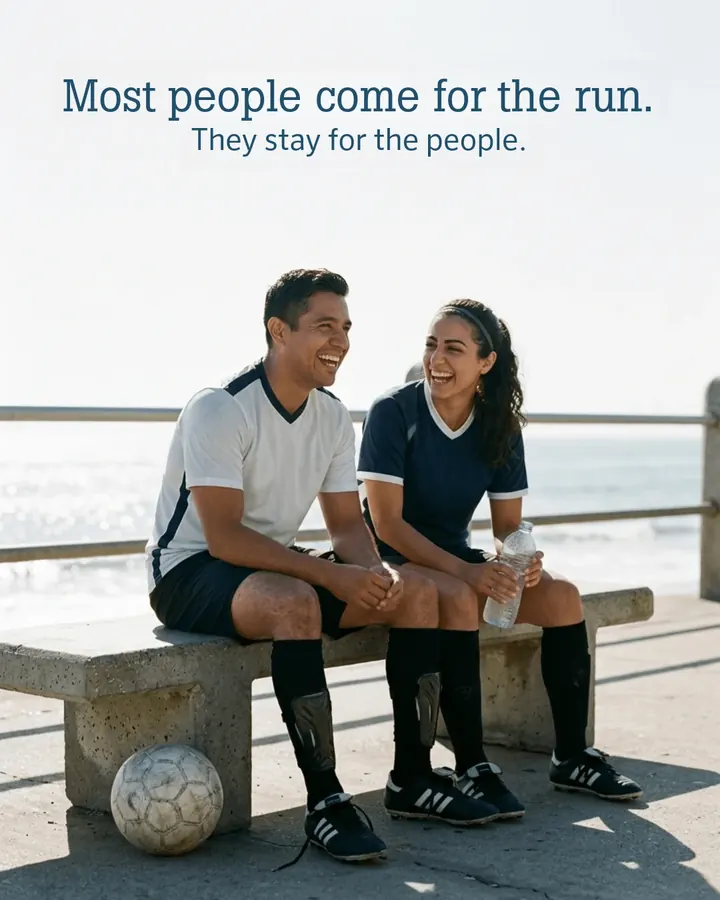 Two club players laughing on a bench by the ocean after a game